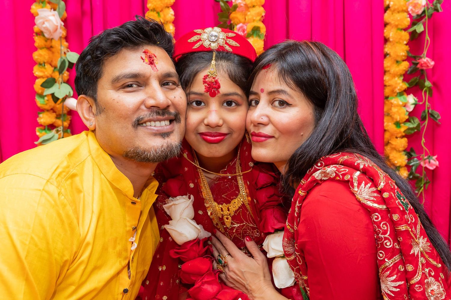 Colorful family portrait against pink backdrop with marigold garlands and traditional attire.