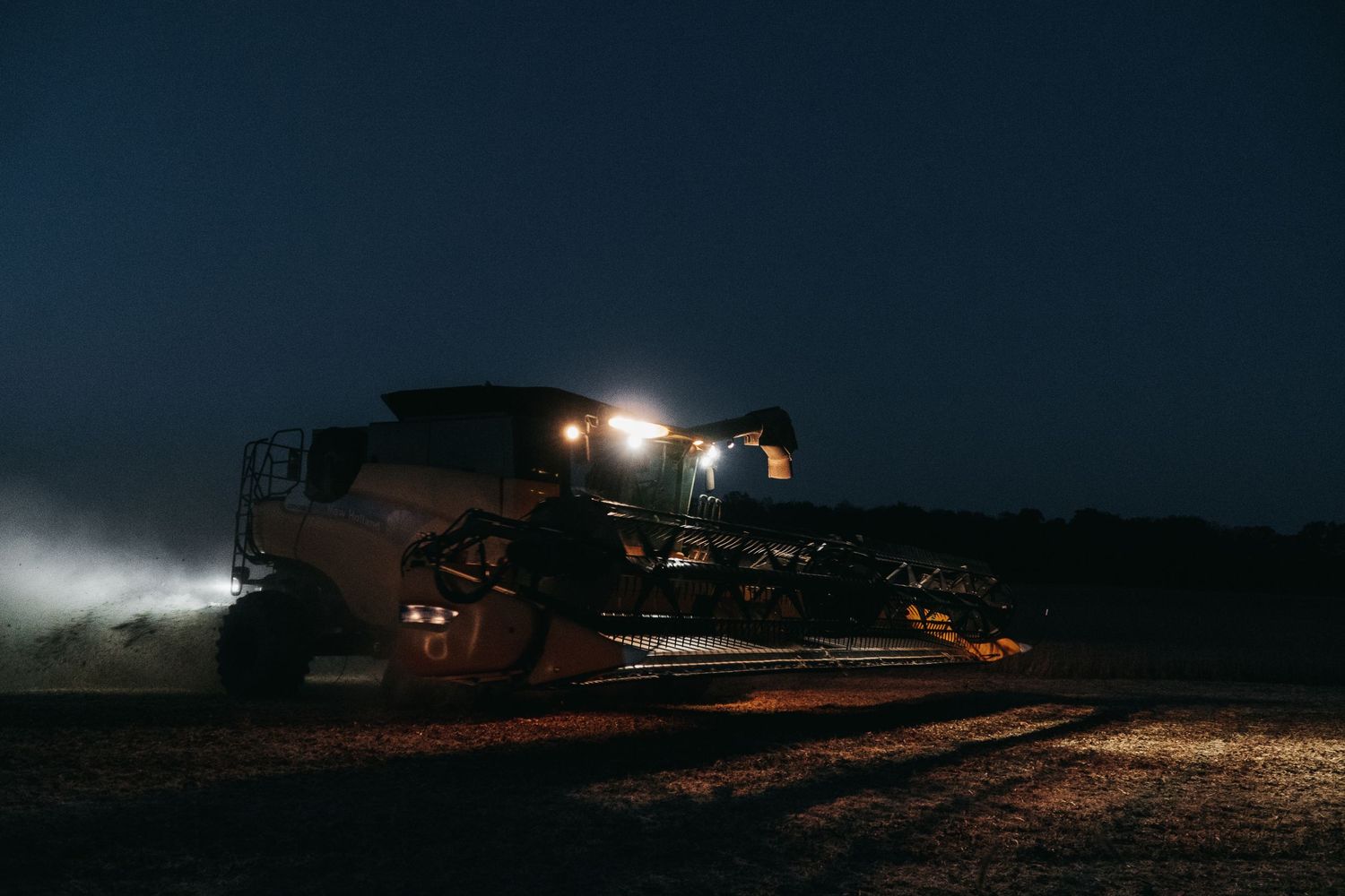 Combine harvester working at night with bright lights illuminating the field.