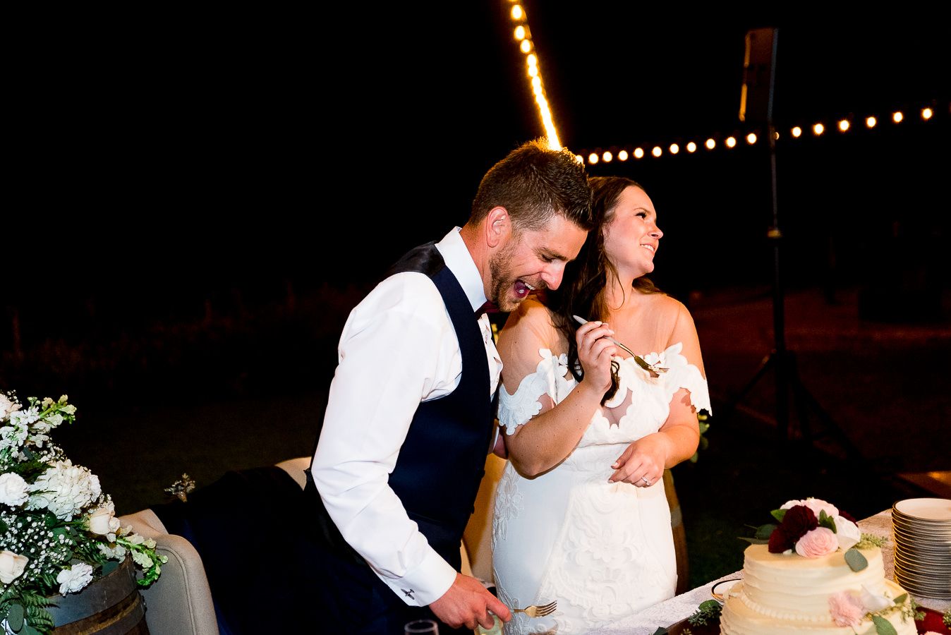 groom laughs as bride feeds him wedding cake at outdoor wedding reception at Pennyroyal Farm