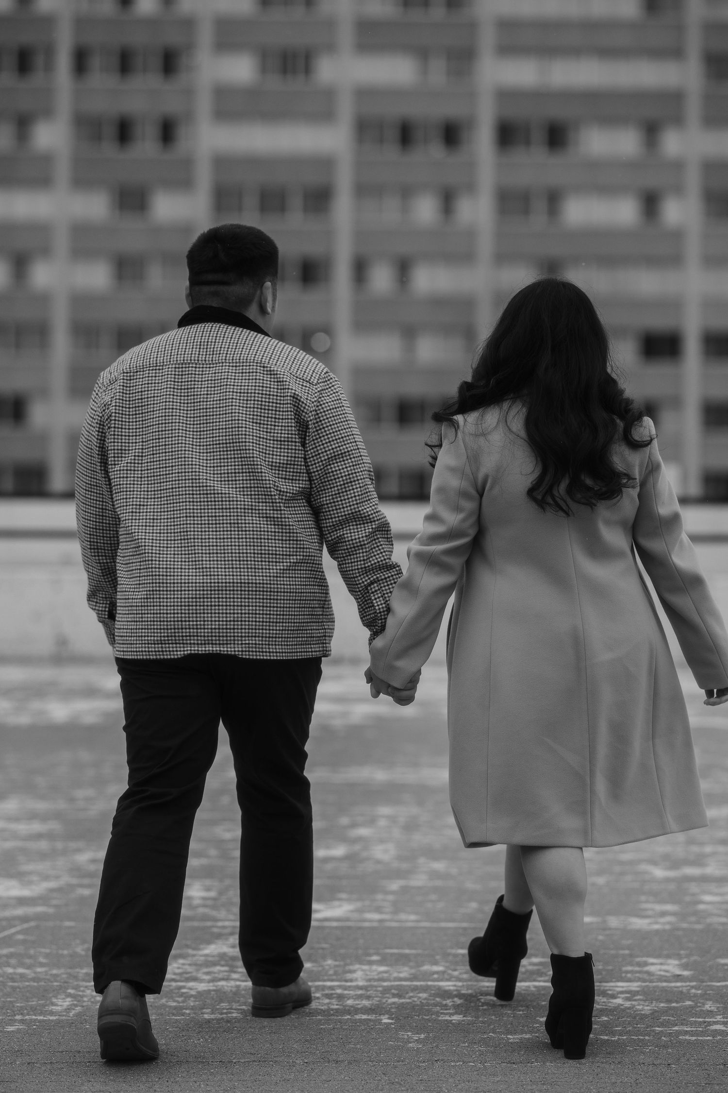 A couple holding hands while walking together in front of an apartment building in black and white photography.