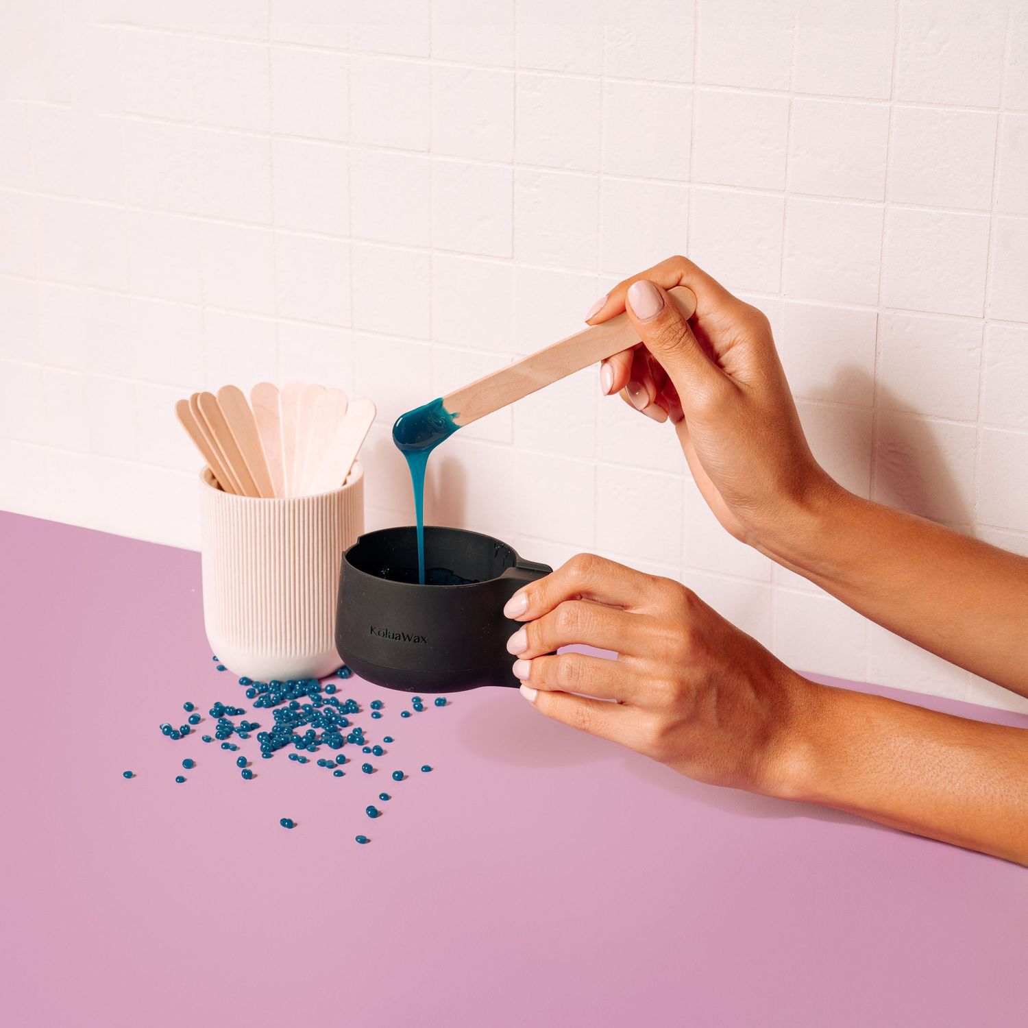 Hands pouring blue crystals into black container on pink and purple surface.