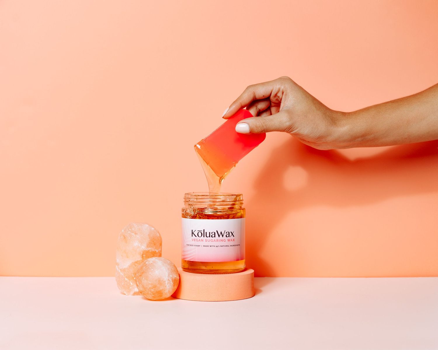 Hand holding red card over skincare product jar on coral surface.