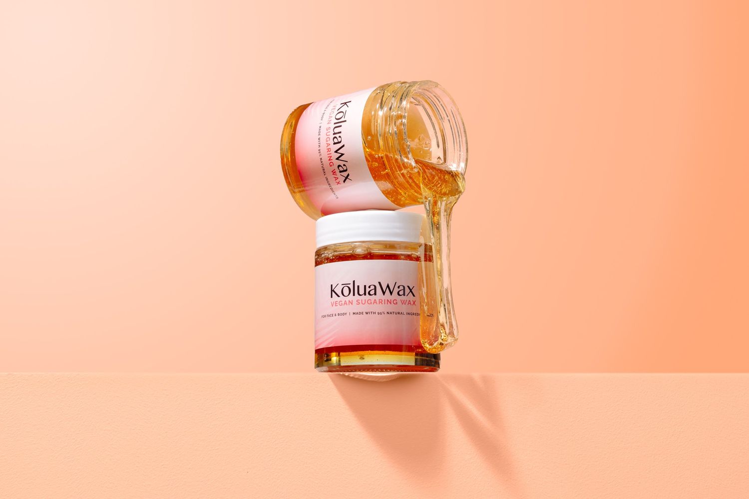 Amber-colored beauty product jar on peach background with dramatic lighting.