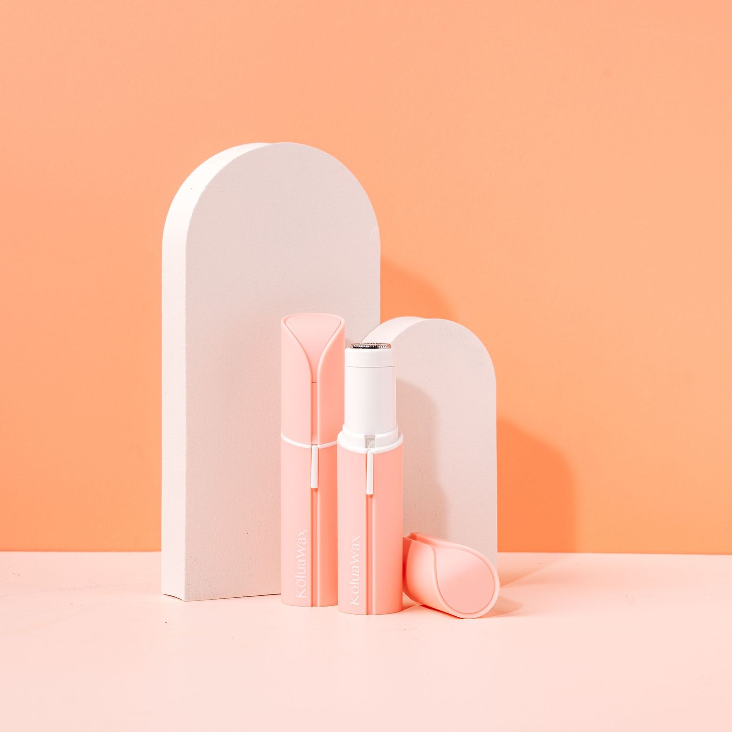 Minimalist pink and white bathroom accessories arranged against a coral colored background.