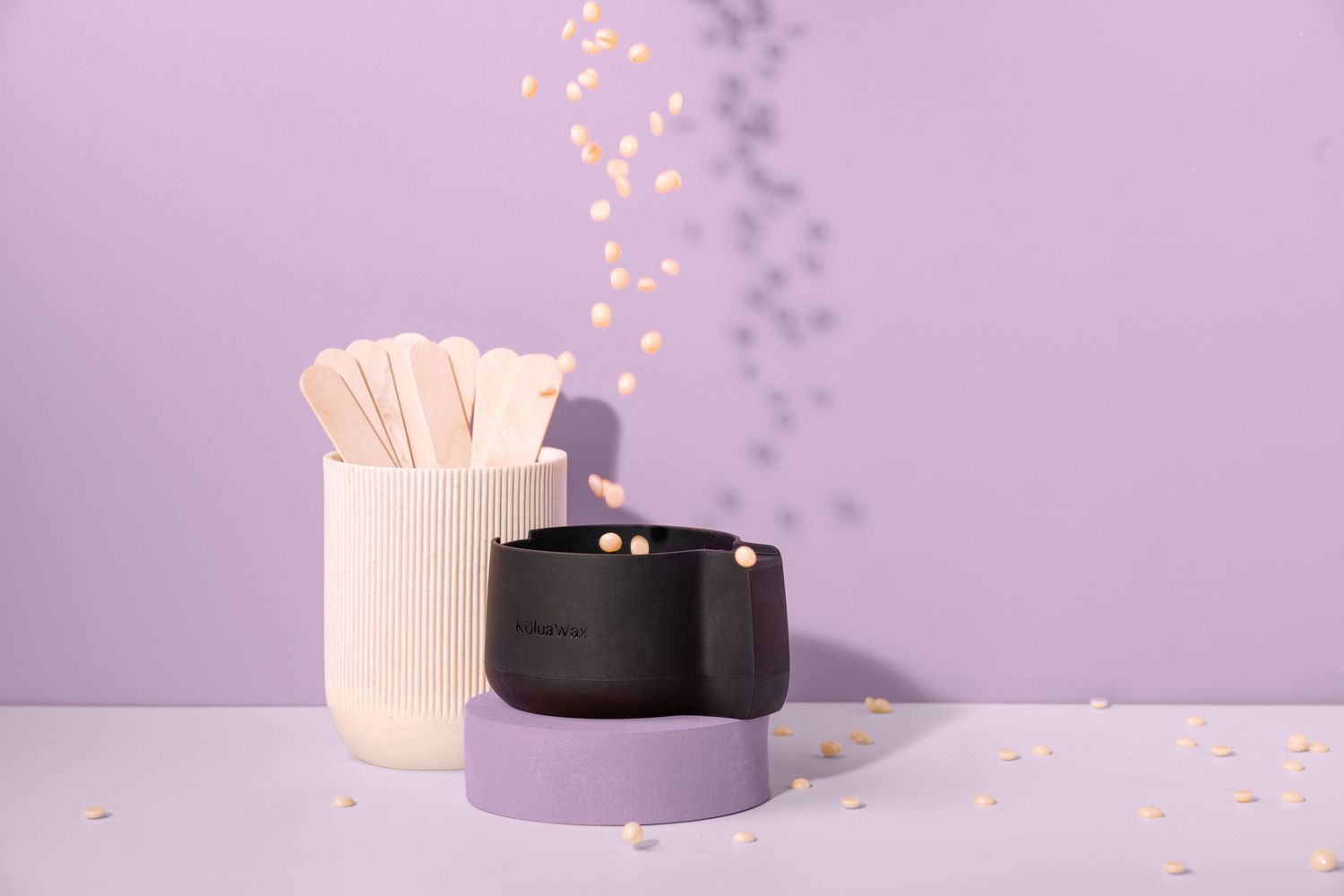 Cotton swabs in a white ceramic holder next to a black and white container against a purple background.