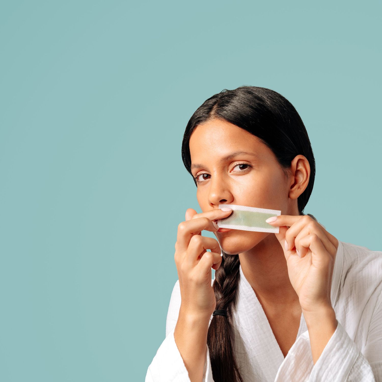 Person in white using skincare product against turquoise background.