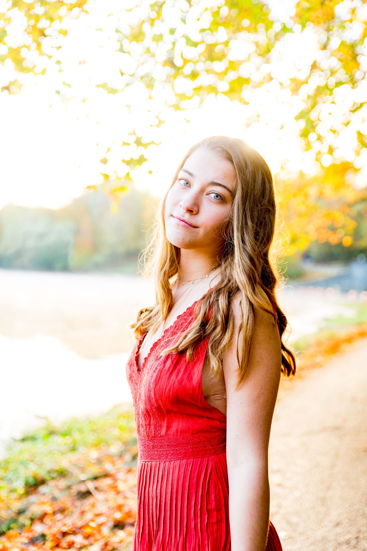 young woman in orange jumpsuit smirks under a yellow tree at Sharon Woods Park at sunrise senior pictures