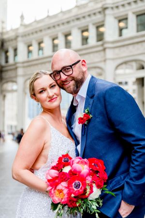 man and woman in navy and silver smiling under Wrigley Building with red flowers after Chicago Elopement