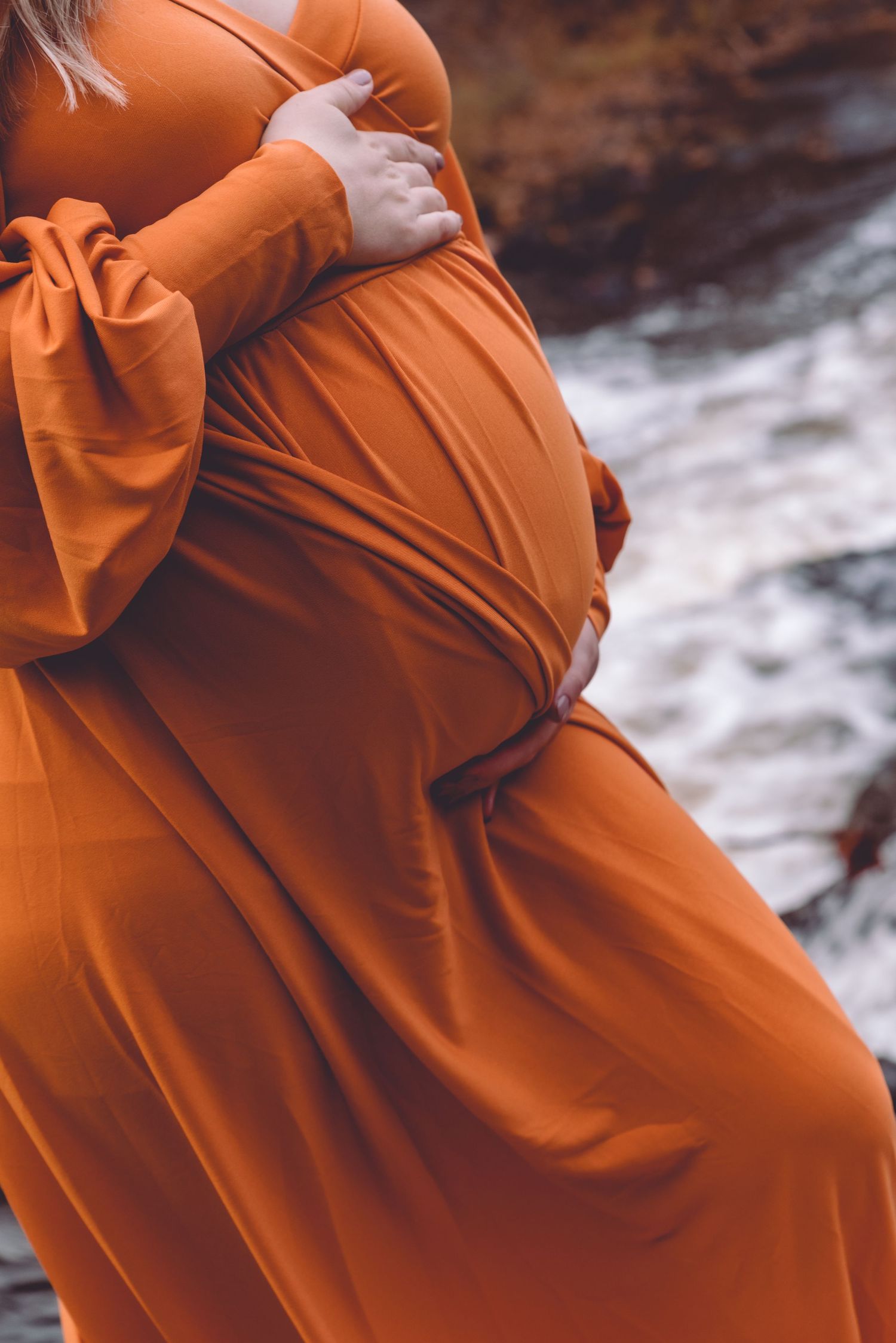 close up of a pregnant woman's belly with flowing water in the background