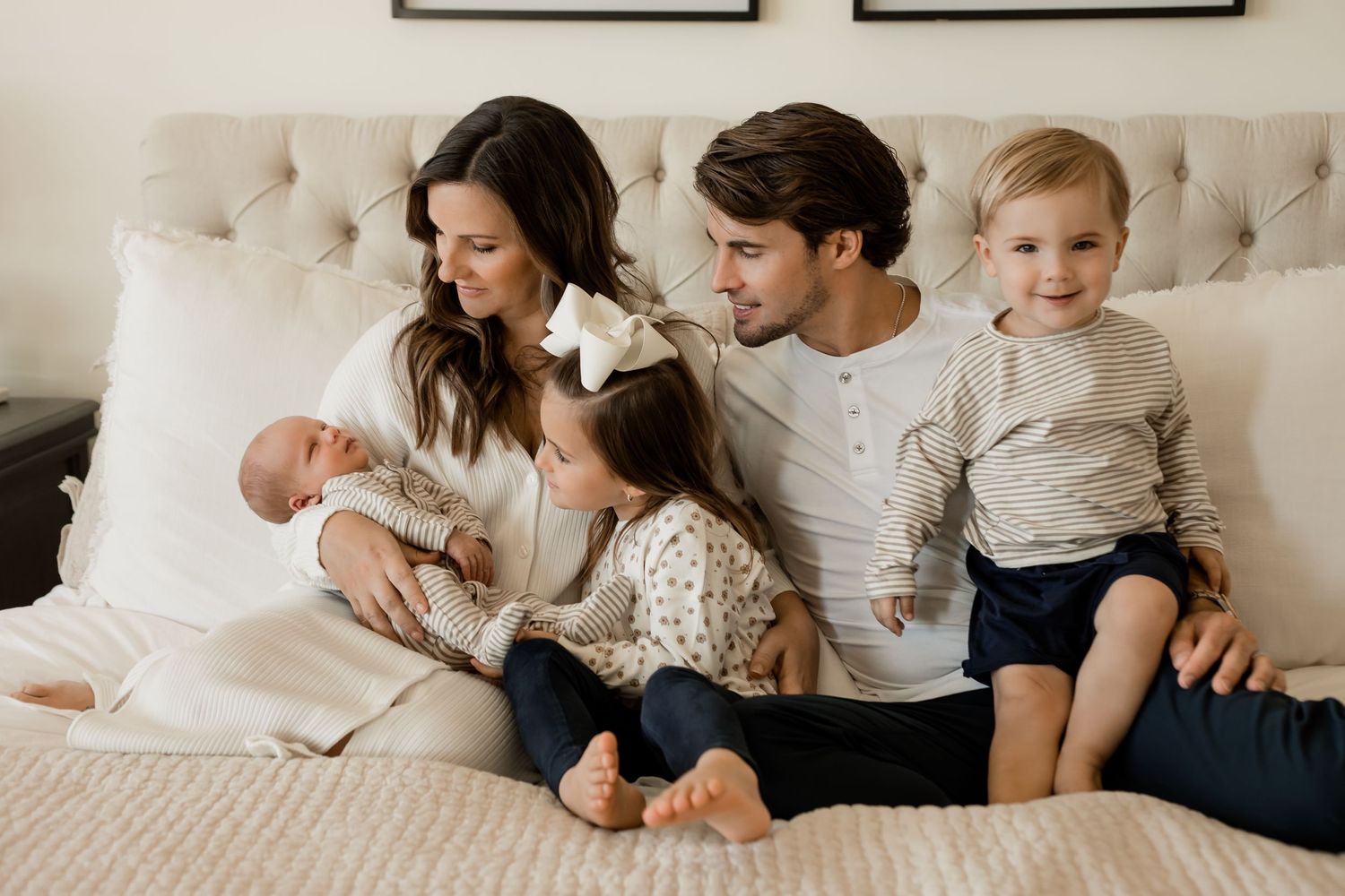 Family of five sitting in their home bedroom for their lifestyle newborn session with kids and baby.