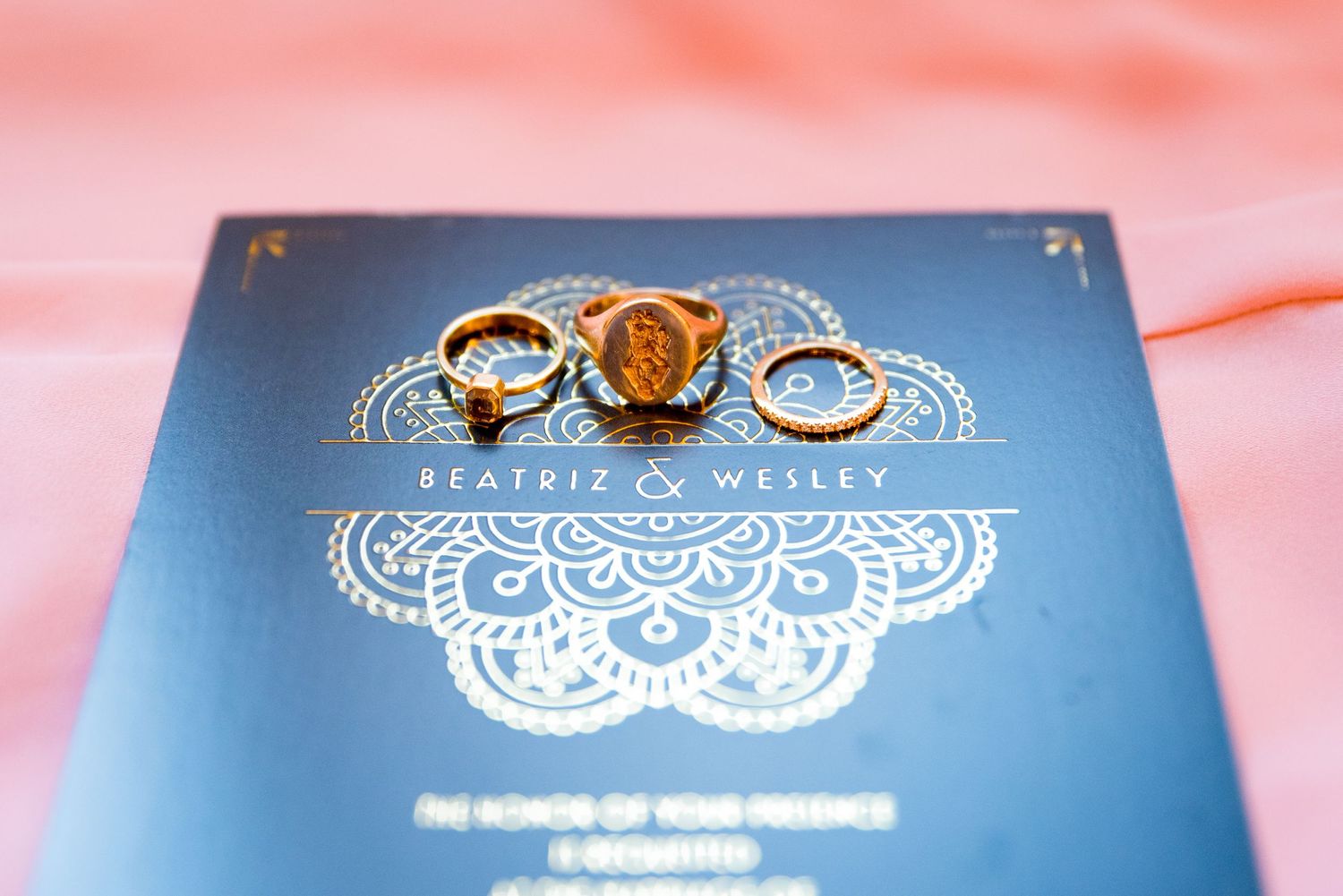 three wedding rings on a green and gold wedding invitation