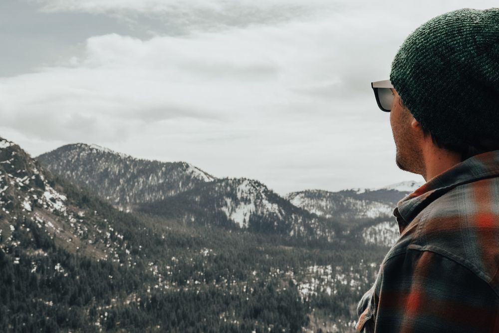 Person in winter hat gazing at snow-covered mountain landscape.