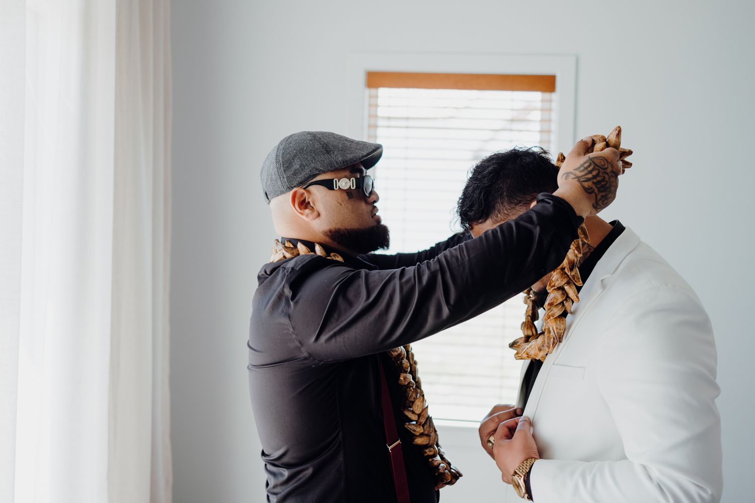 Two people in formal attire help adjust traditional lei garlands before a ceremony.