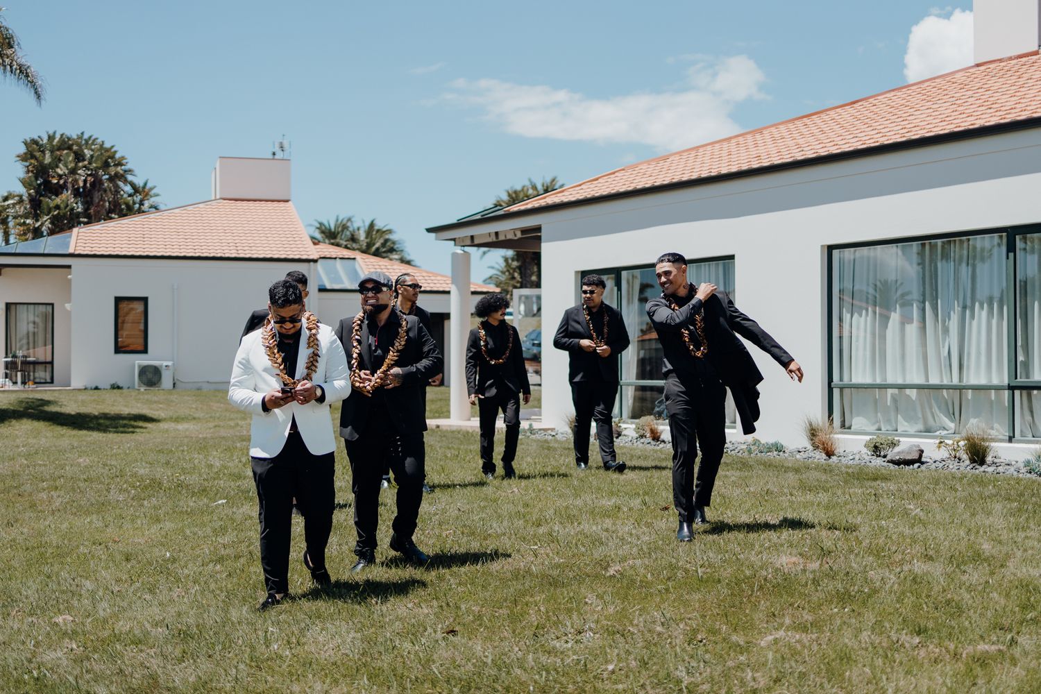 Groomsmen in formal attire enjoying a playful moment outdoors near white buildings.