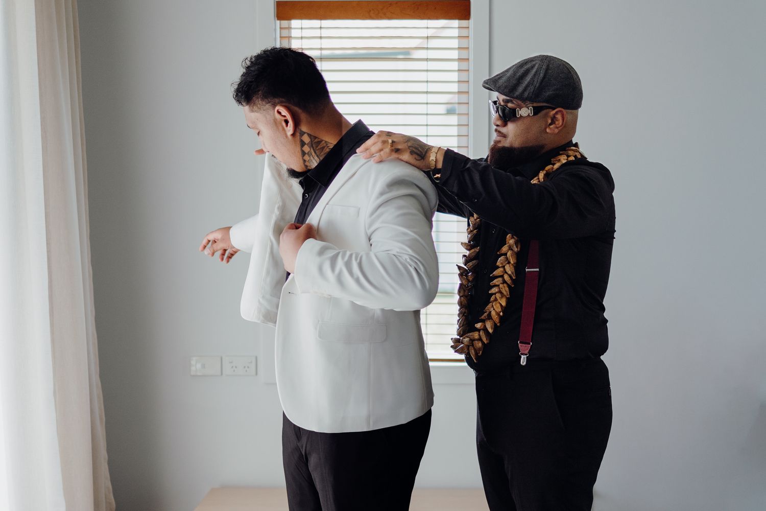 Two people getting ready, one helping adjust the other's formal attire.