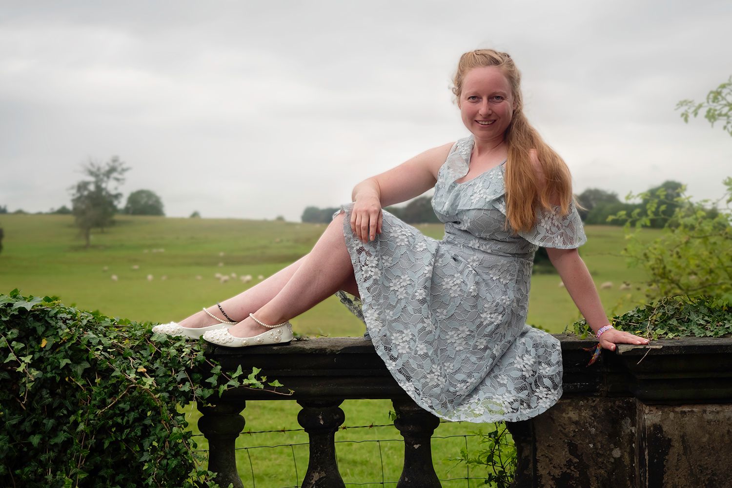 Self portrait sat on wall in blue dress in front of countryside