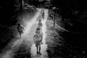 Environmental portrait of Akha Tribe children running after truck along road