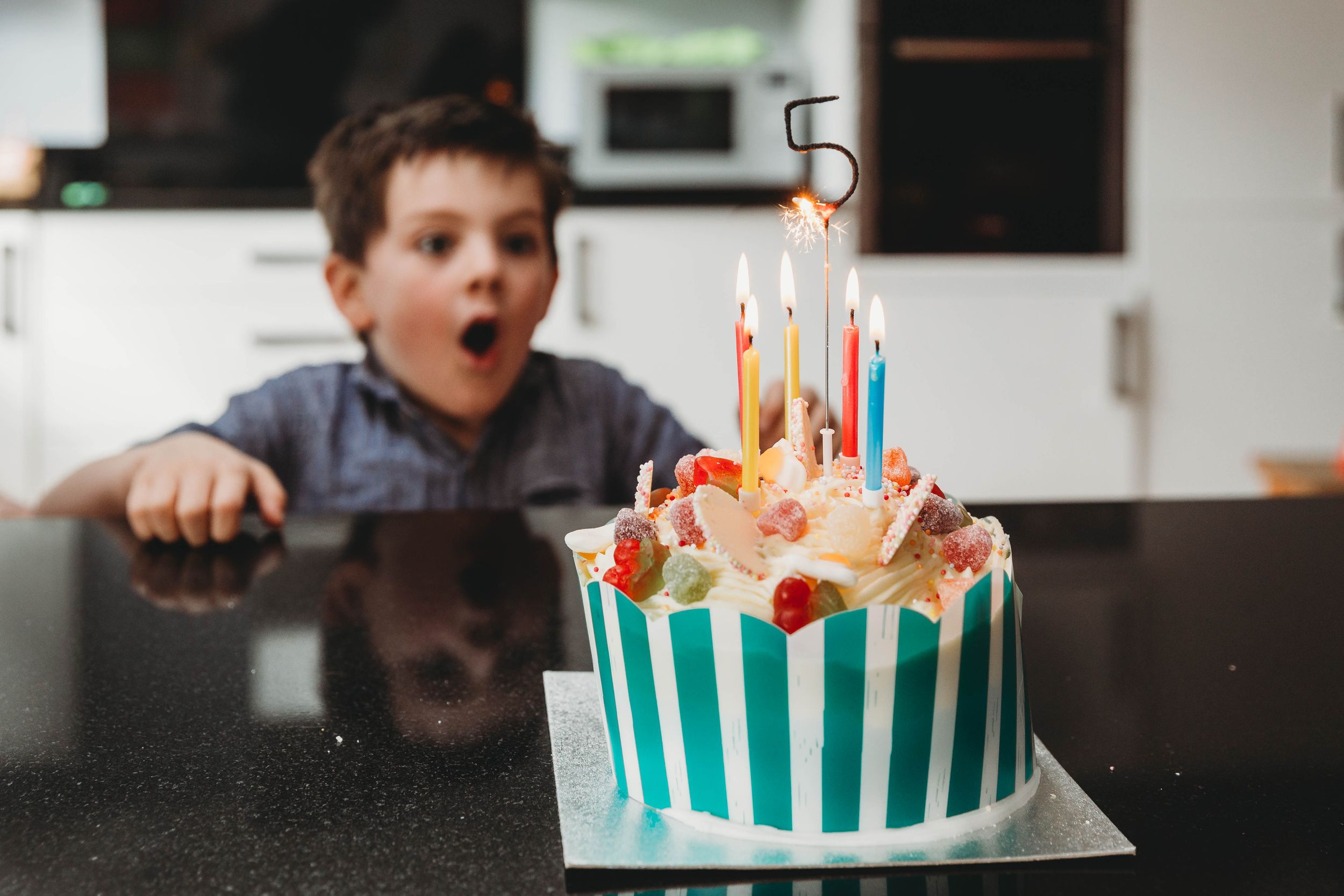 five years old boy shocked seeing birthday cake with sparkler topper