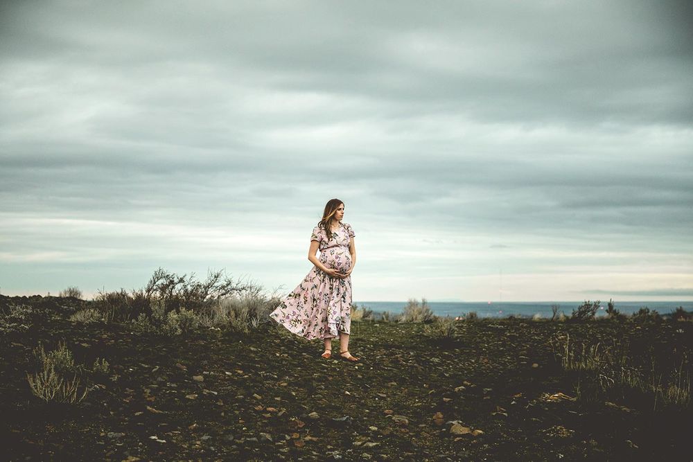 expectant mother is standing and looking off to the side while she holds her baby bump