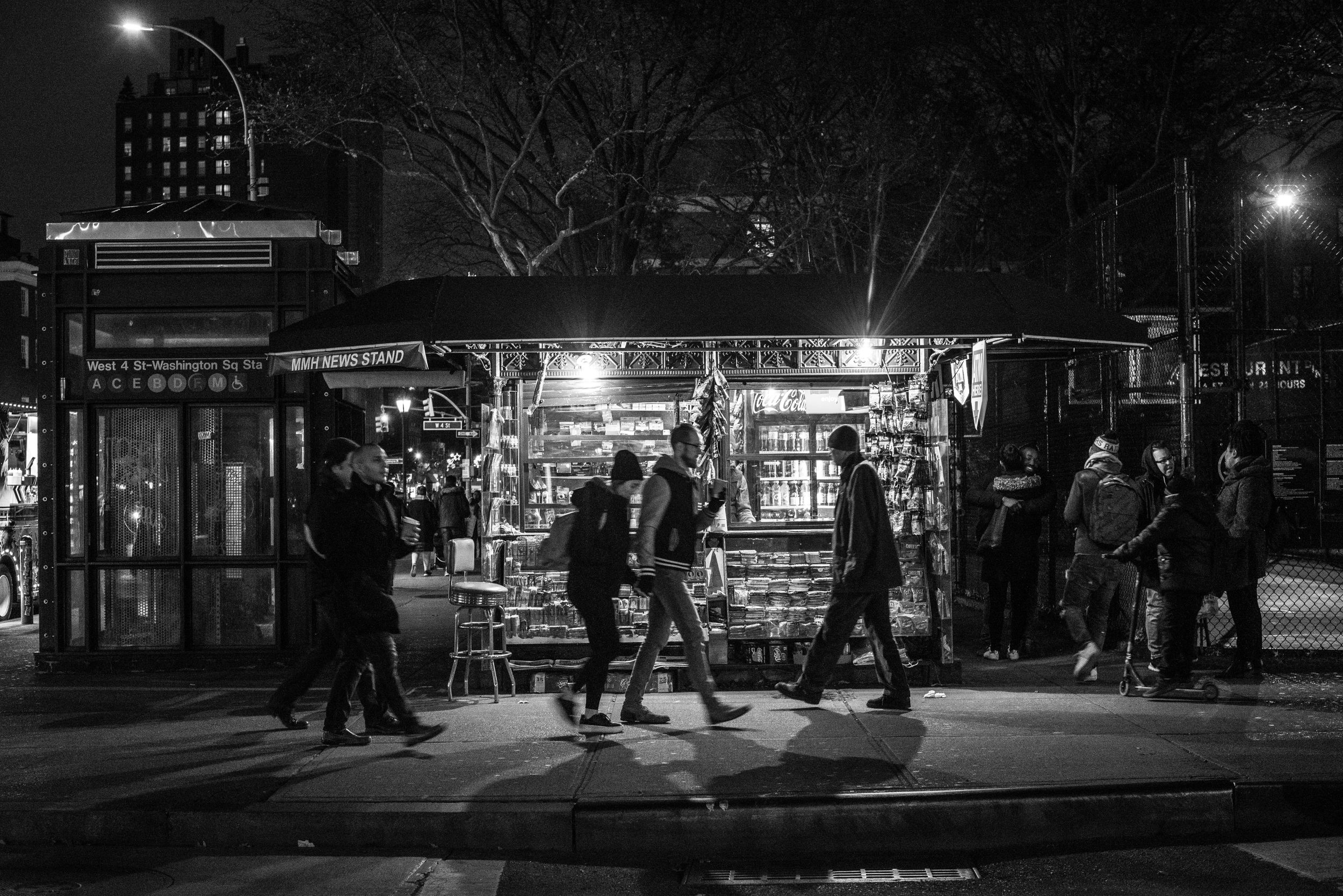 People walking past Greenwich Village newsstand at night in NYC