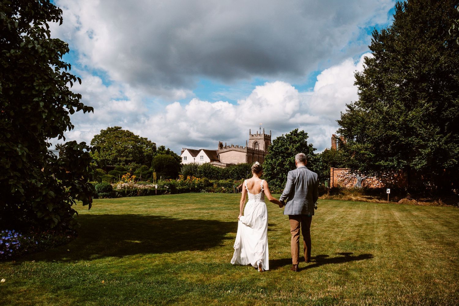 bride and groom walking across lawn holding dress off the grass to avoid staining from berries