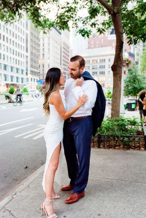 man with suit over his shoulder looking at woman in white dress in front of Flatiron Building NYC engagement photos