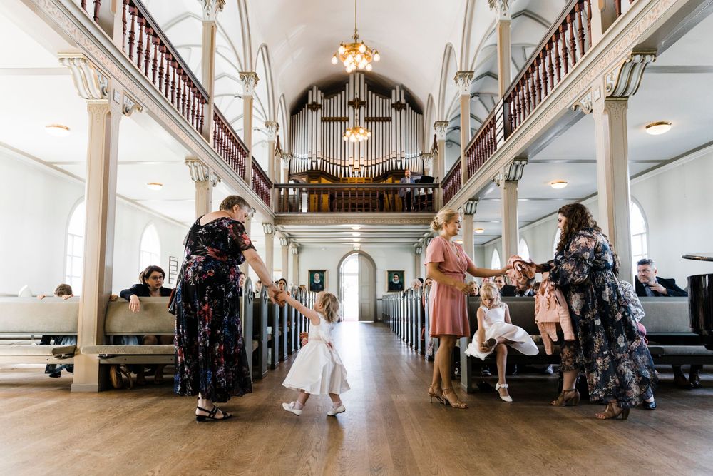 Wedding party members stand in a historic white church interior with grand organ pipes and wooden pews.