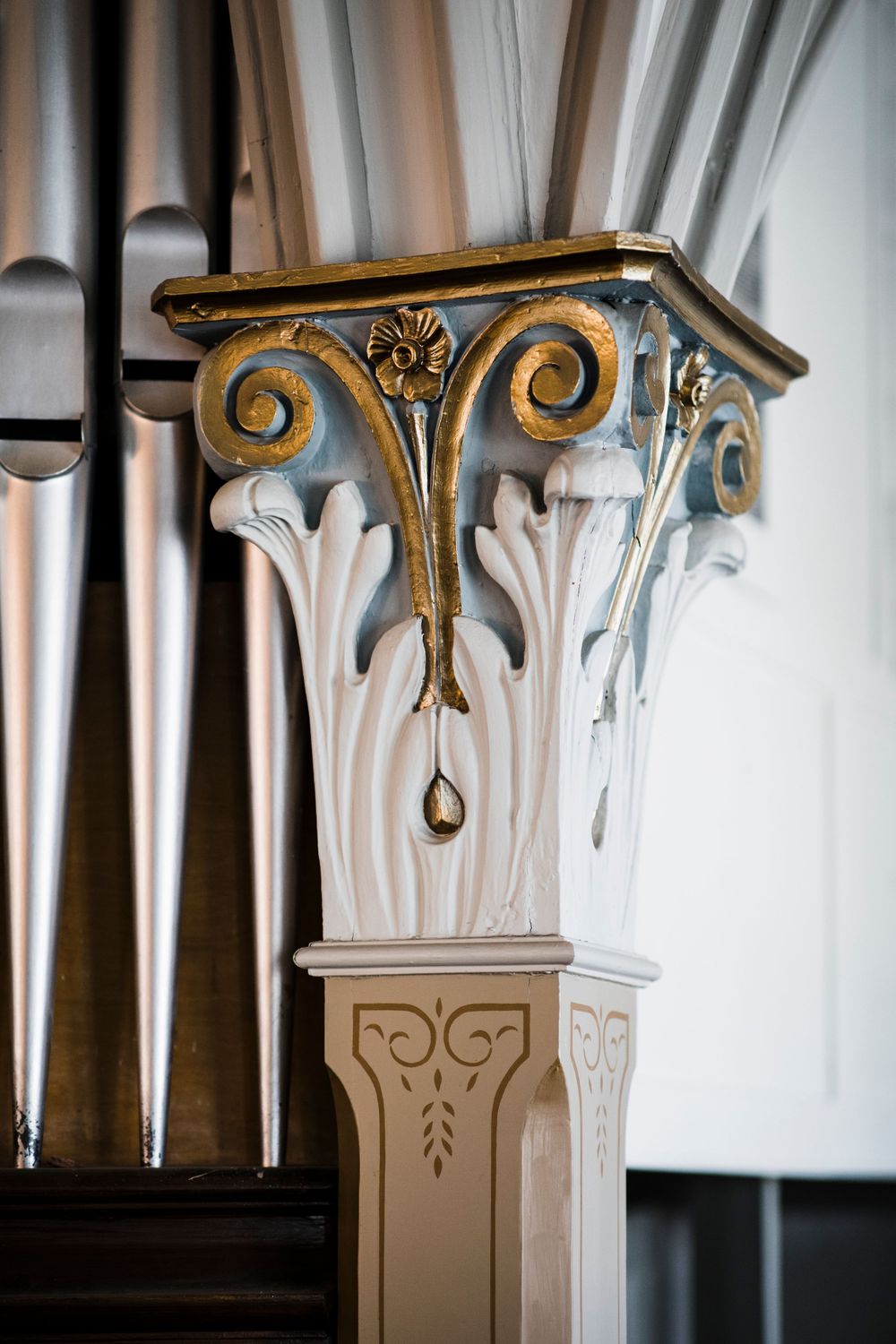 Ornate gold and white architectural detail of a Corinthian column with scrollwork and floral motifs.