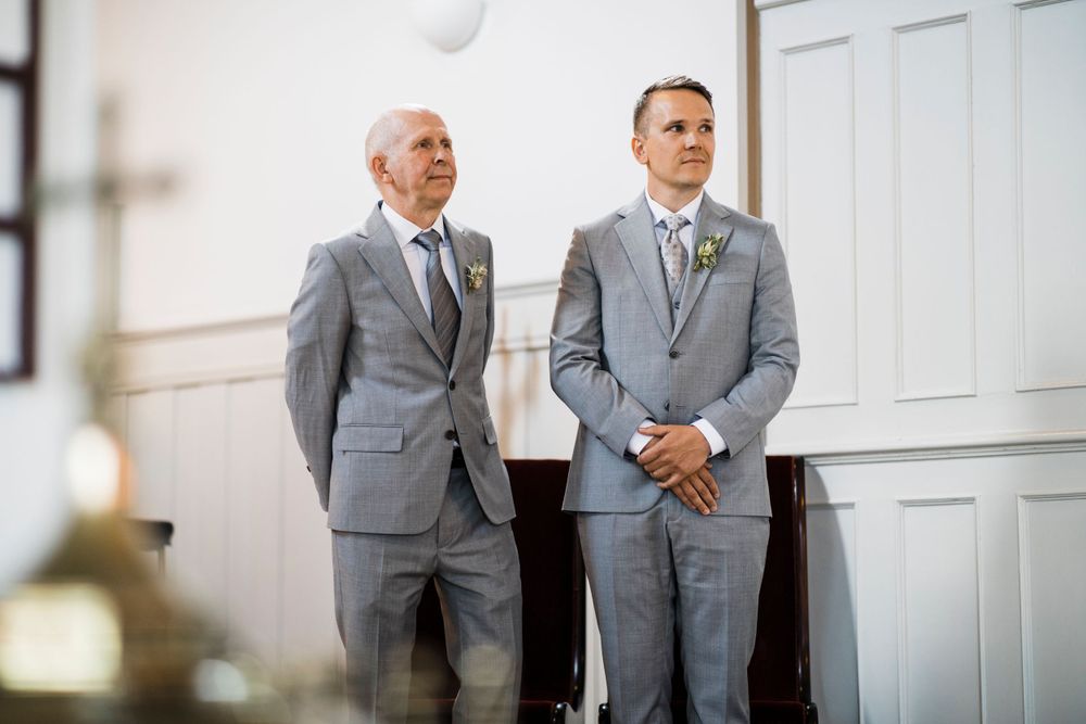 Two men in matching grey suits stand side by side in a traditional church setting.