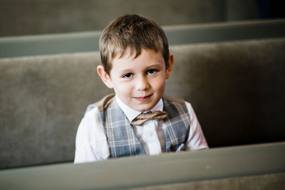 Young child in plaid vest and bowtie sitting in church pew.