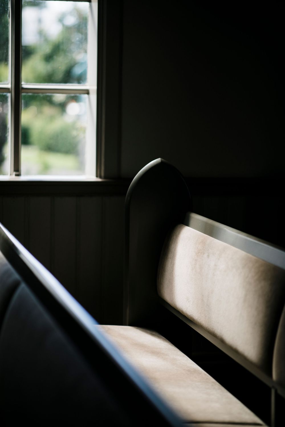 Empty church pew with window light casting shadows in a moody composition.