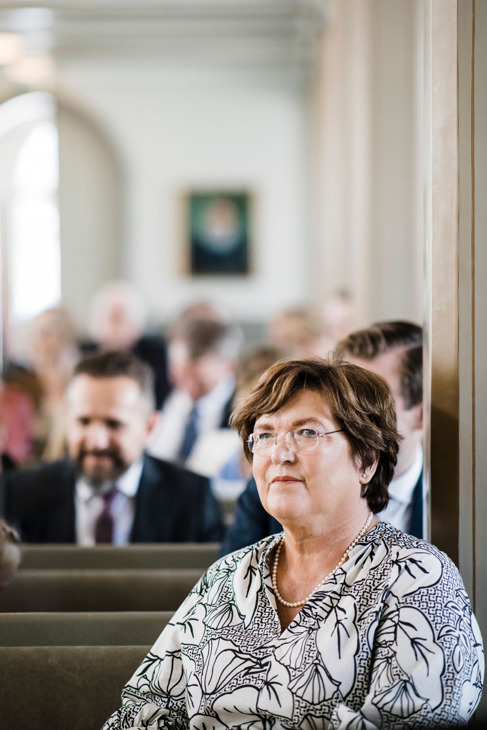 Wedding guest seated in church pew wearing floral print dress during ceremony.