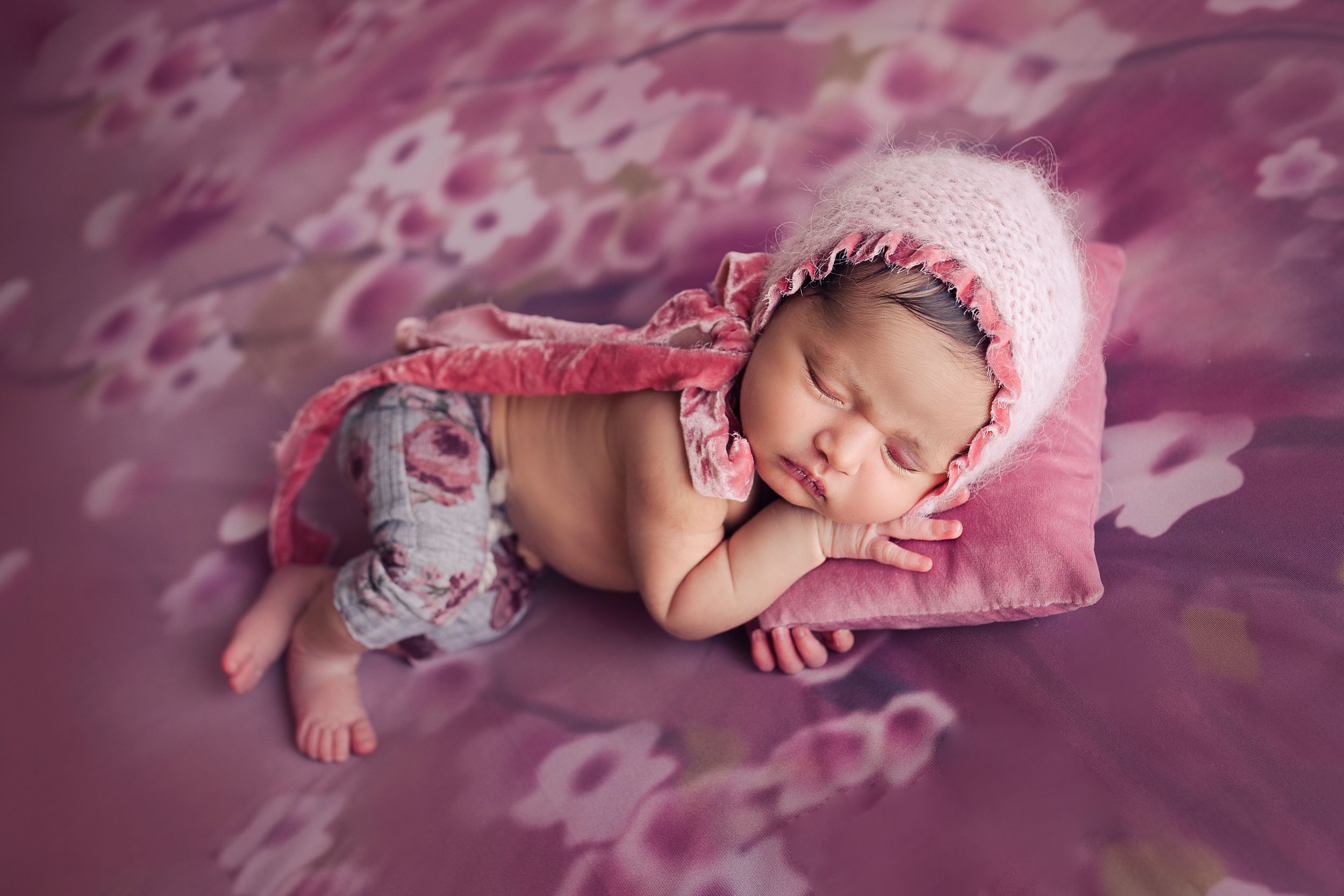 Baby girl side lay with pillow and wearing pink bonnet