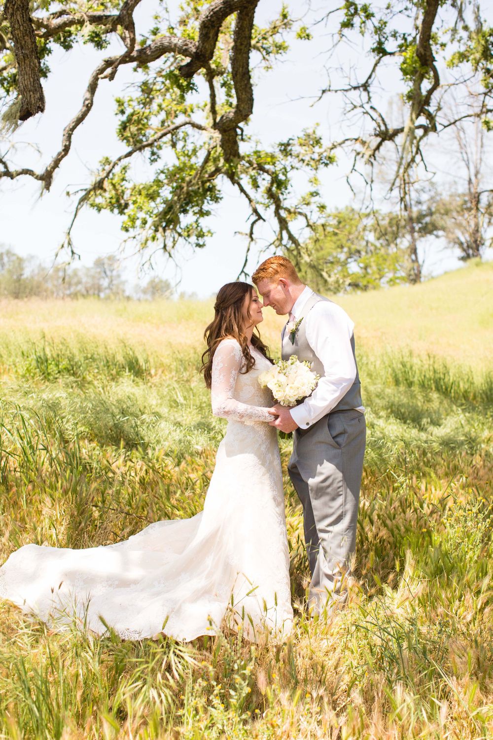 Bride and groom facing each other in an open field under an oak tree