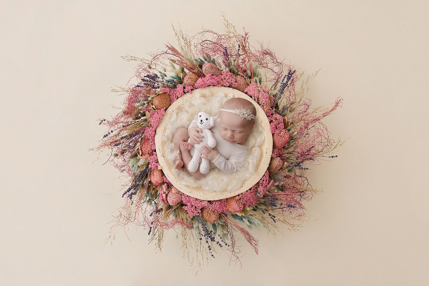A baby girl in a floral next holding a teddy taken by Little Brown Rabbit Photography in Perth newborn studio