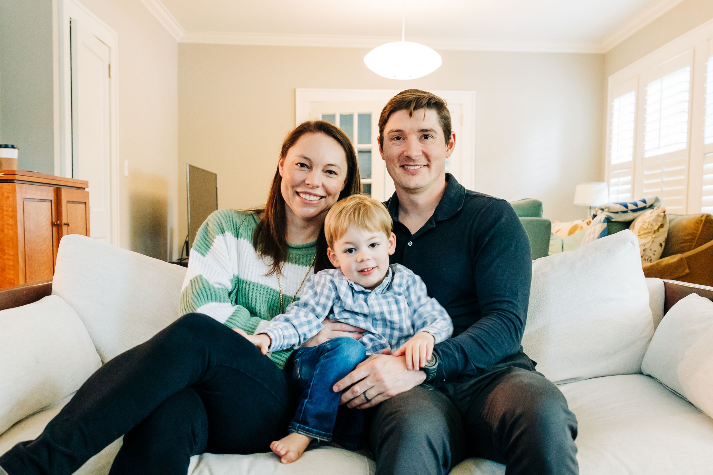 Family of 3 smiling at the camera on their couch