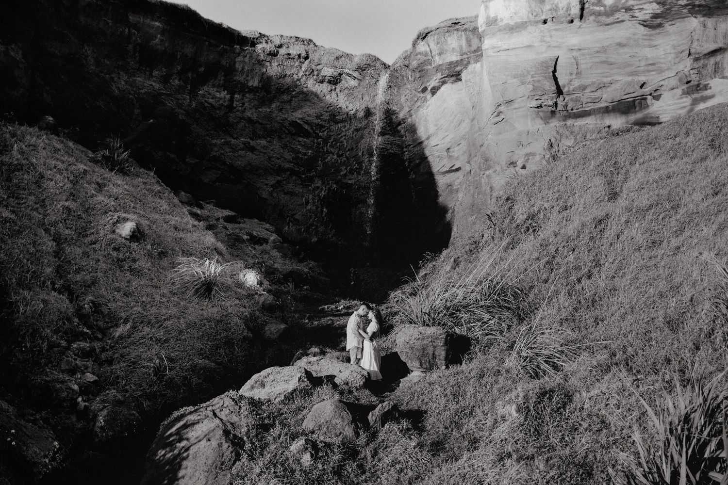 Couple and waterfall in their engagement shoot in Karioitahi Beach with Apertured Media-Auckland Wedding Photographer
