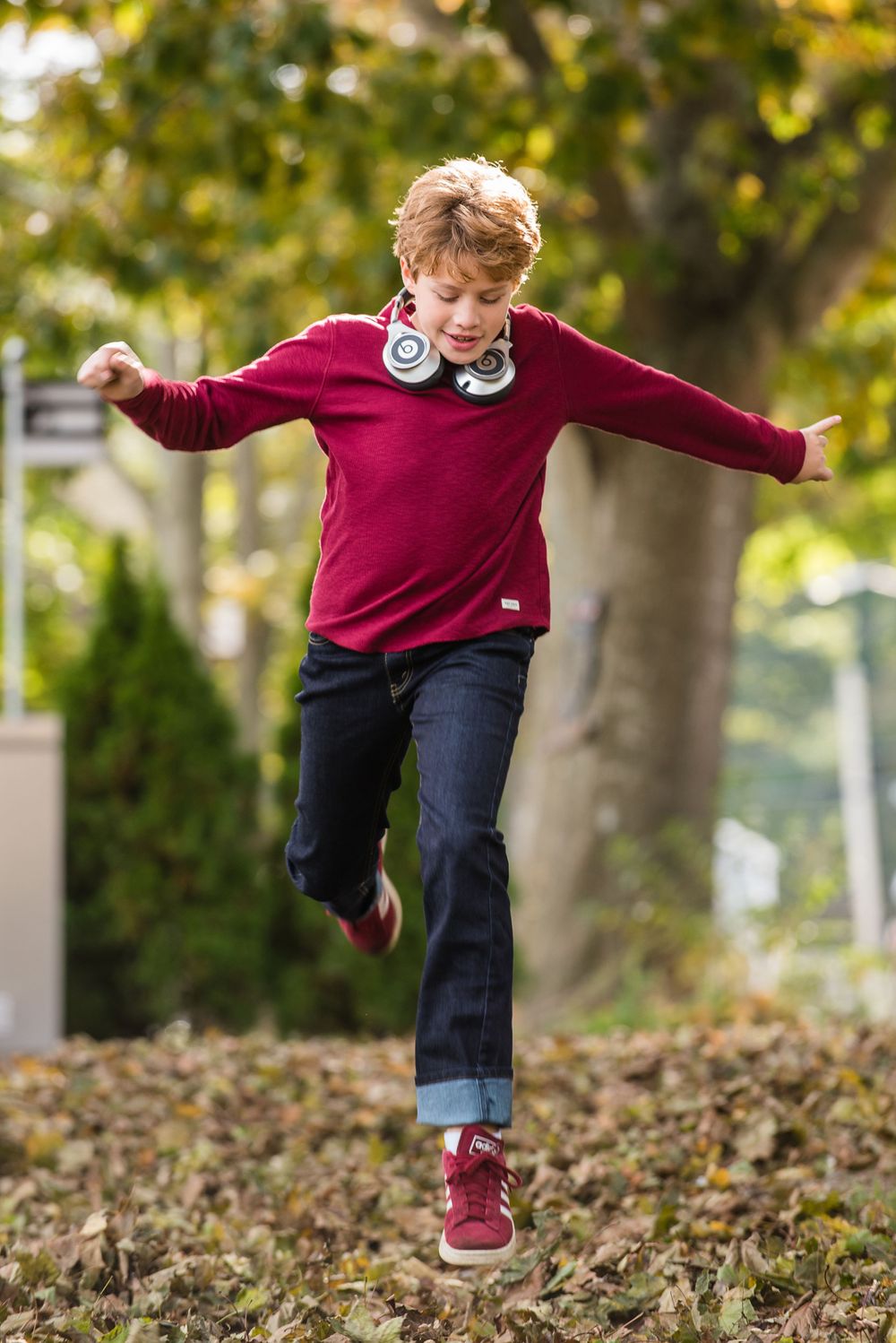 Tween male model wearing headphones jumping through leaves