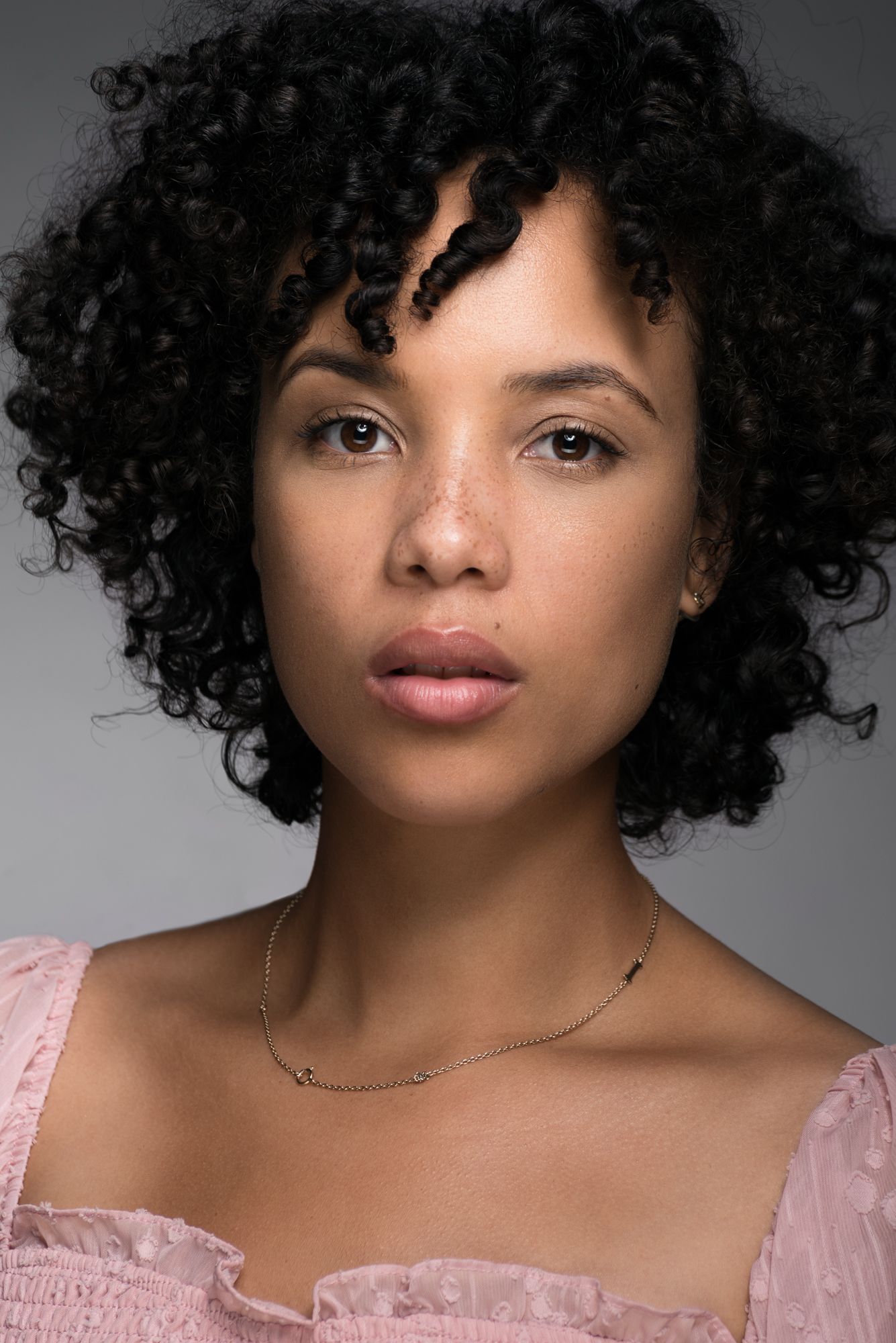 Actor headshot against a grey background, with a white top, in studio by Caribbean Photographer Logan C Thomas