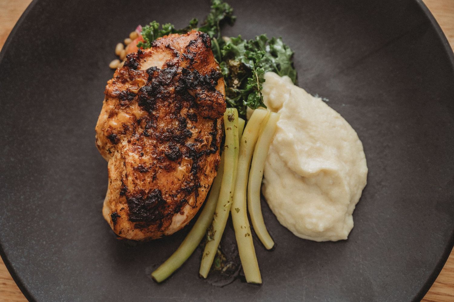 Grilled chicken breast with potatoes and vegetables beautifully plated on a black dish. SIX84 Photography, Food Photography, Sydney
