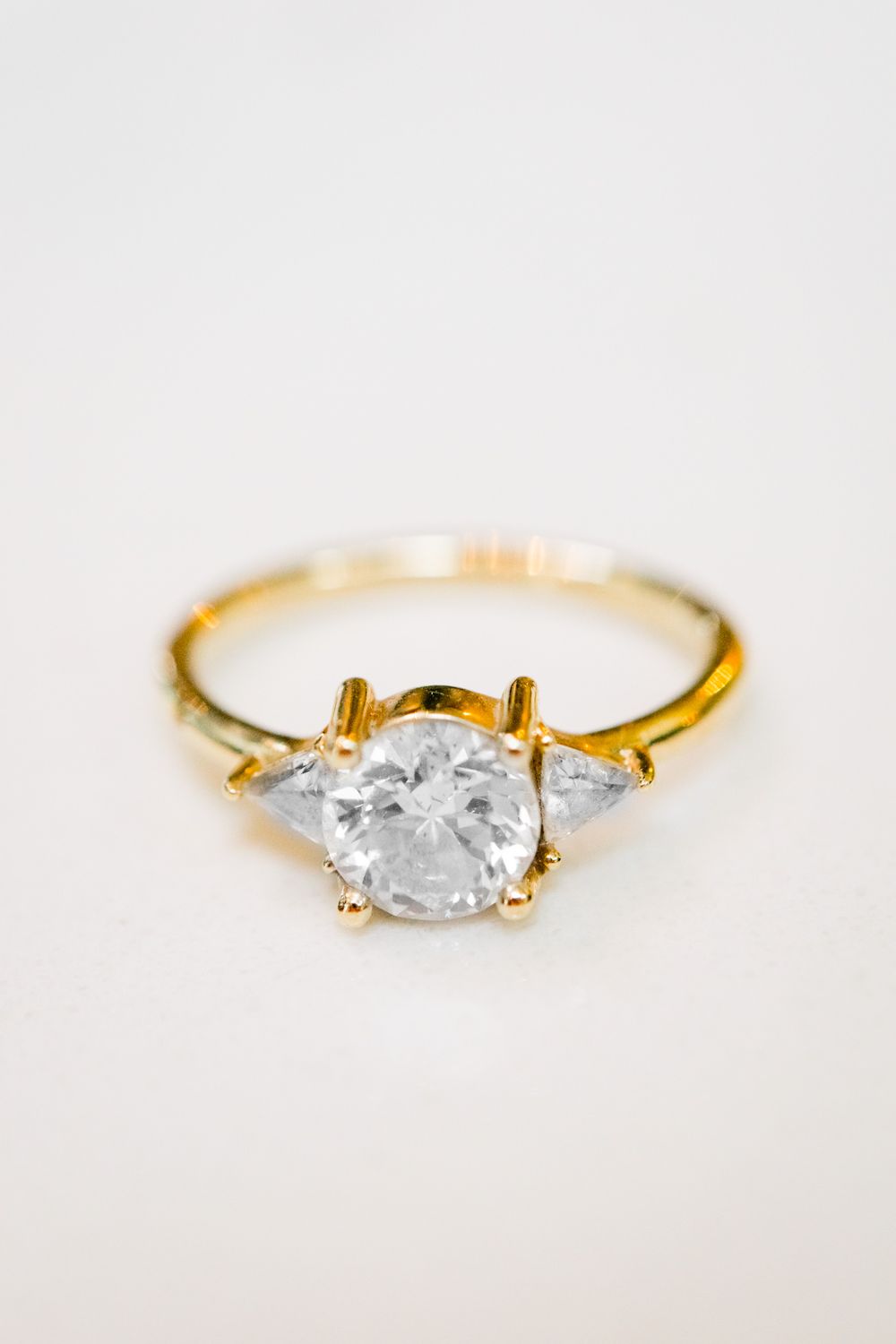 gold band engagement ring with round diamond and two triangle side stone diamonds
