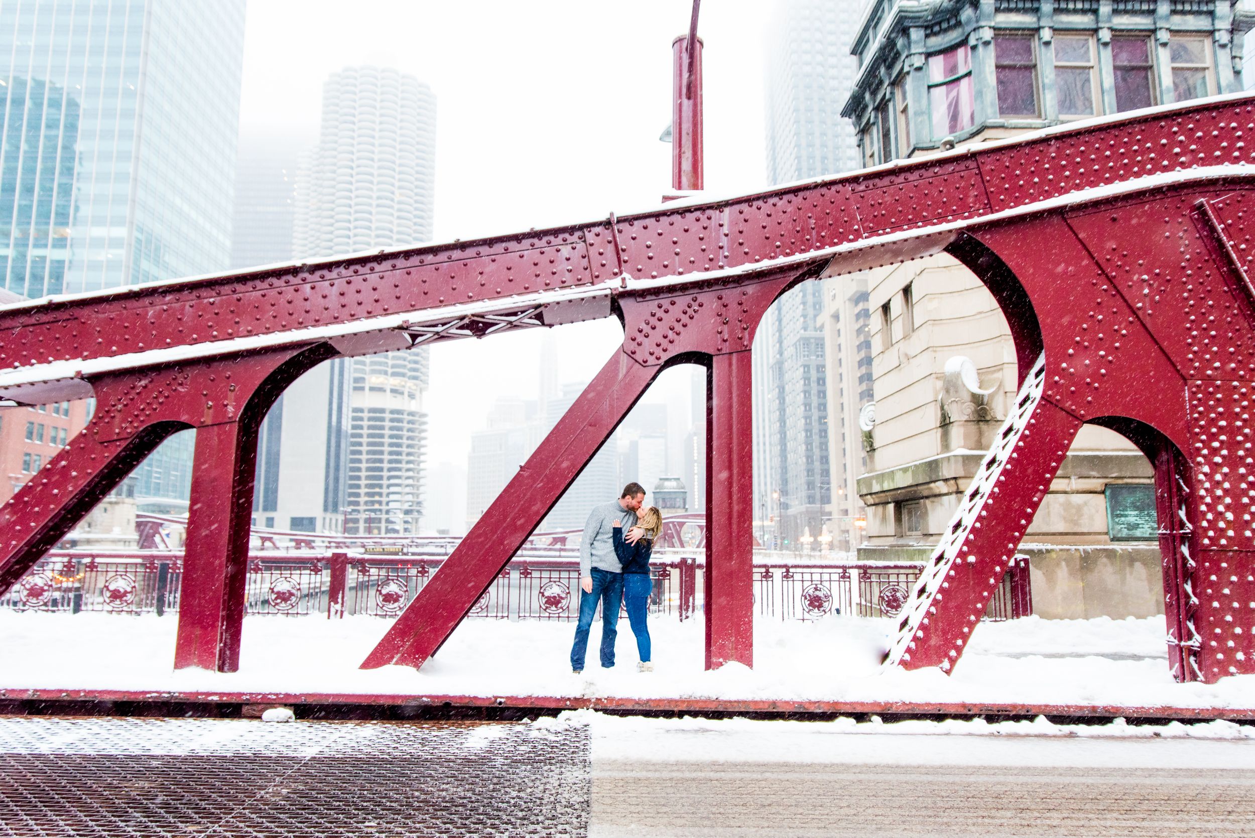 engaged couple in Chicago standing under bridge kissing in the snow