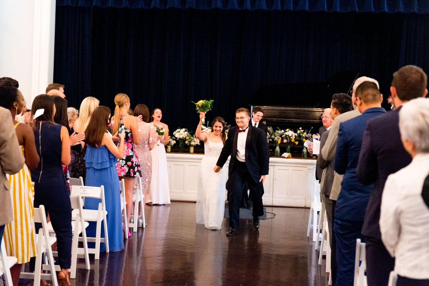 bride raises bouquet in the air and walks down the aisle with groom after just getting married
