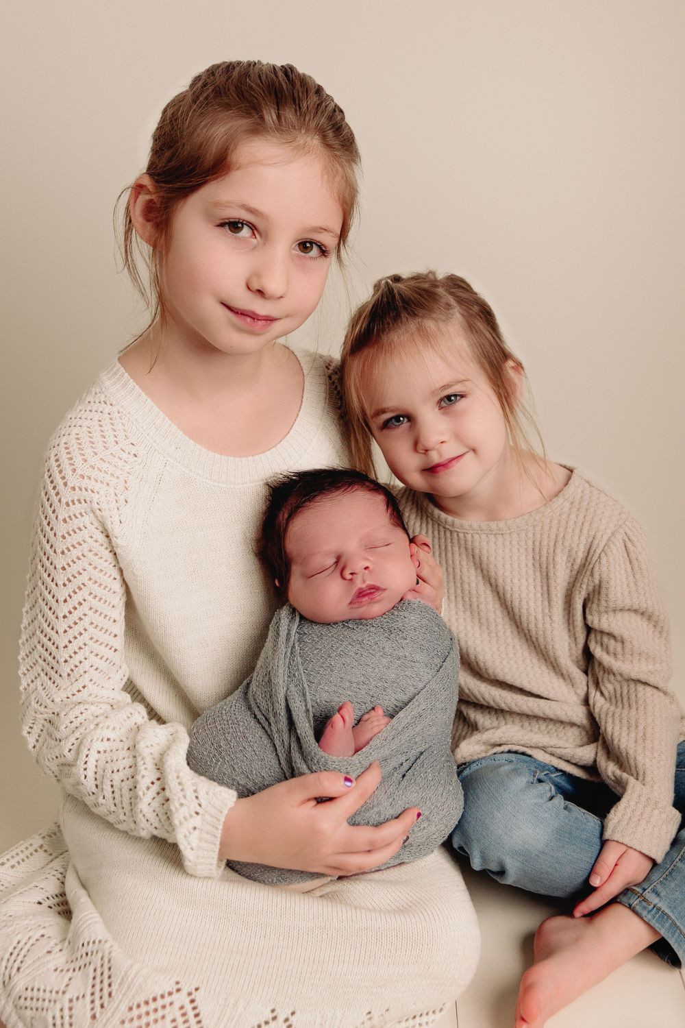two children holding newborn baby brother in blue wrap