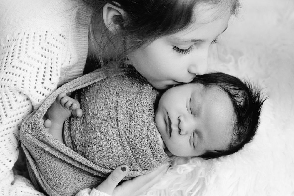 black and white big sister kissing baby brothers cheek