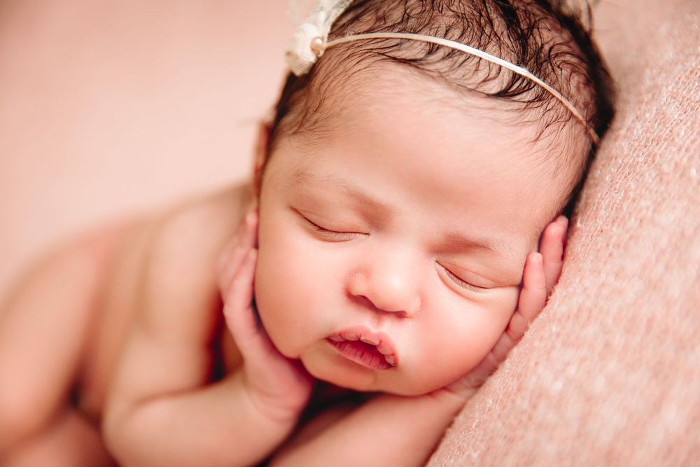 newborn girl on pink blanket one hand on each cheek