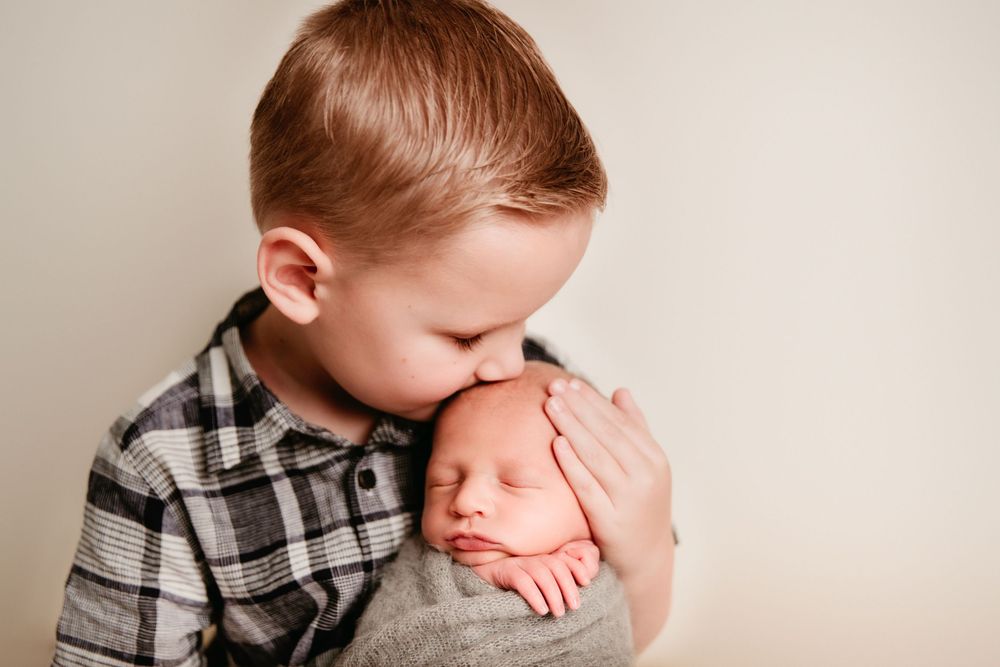 big brother holding newborn boy kissing top of head