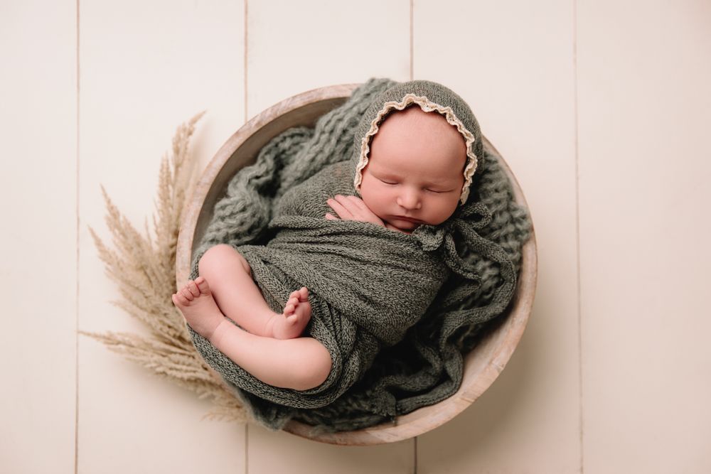 aerial angle of newborn girl white bowl swaddled in a sage wrap and matching bonnet