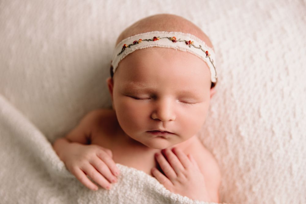 baby girl tucked in sleeping on white blanket wearing boho headband