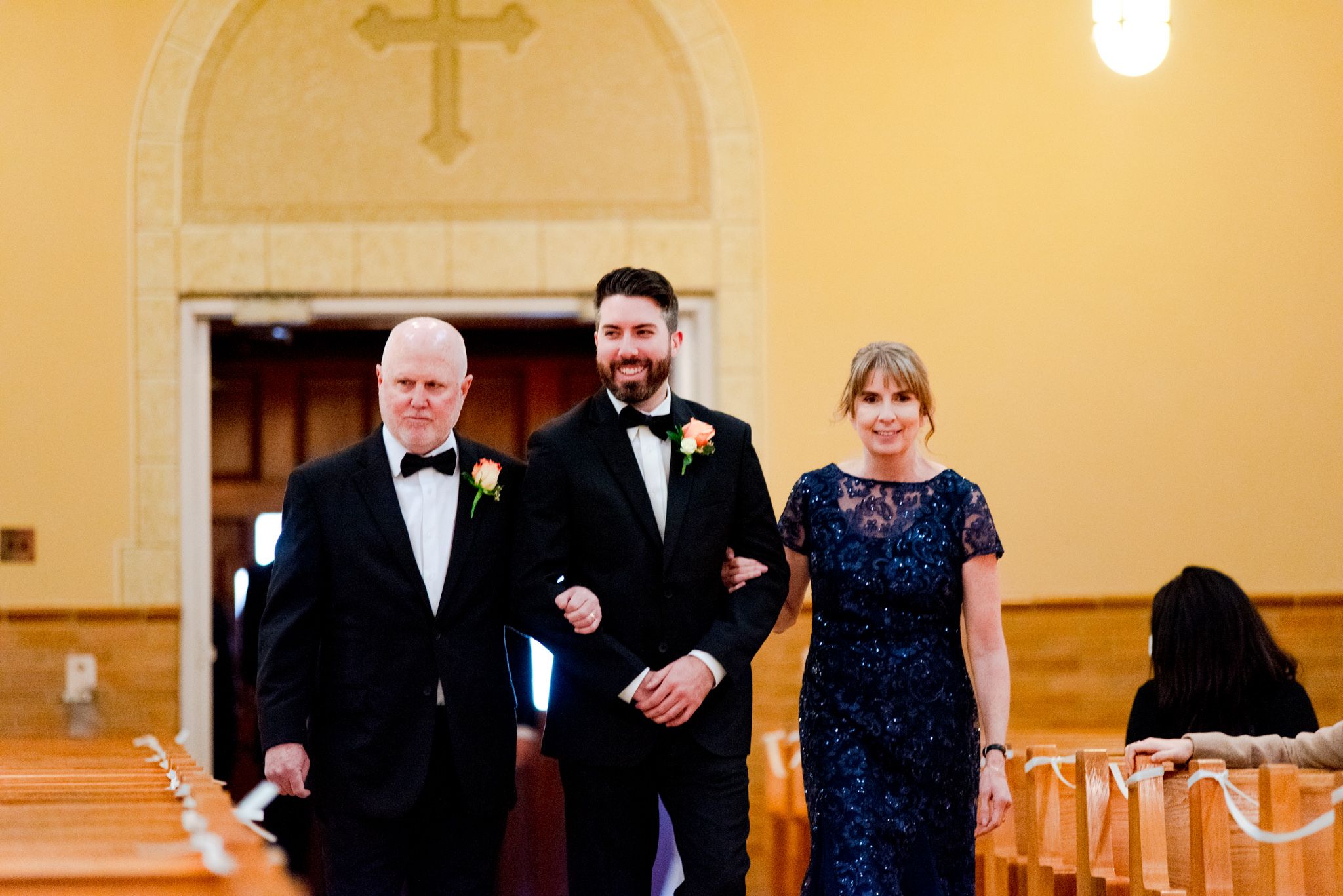 groom walking down the aisle with dad on let and mom on right in blue sparkly dress